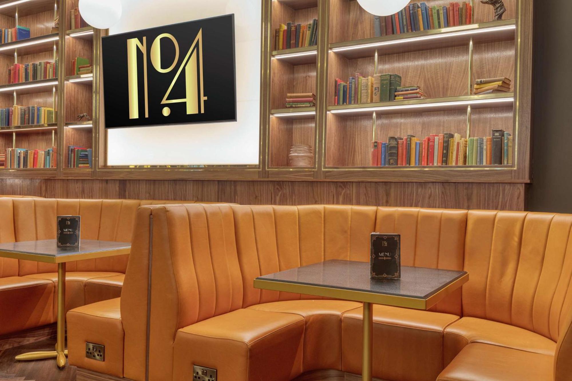 โรงแรมฮิลตัน เบลฟาสท์ เบลฟาสต์ ภายนอก รูปภาพ The photo shows a cozy interior space featuring a stylish seating area. There are plush, orange leather booths with an elegant design, arranged around small tables. The background includes a wooden bookshelf filled with a variety of colorful books. A