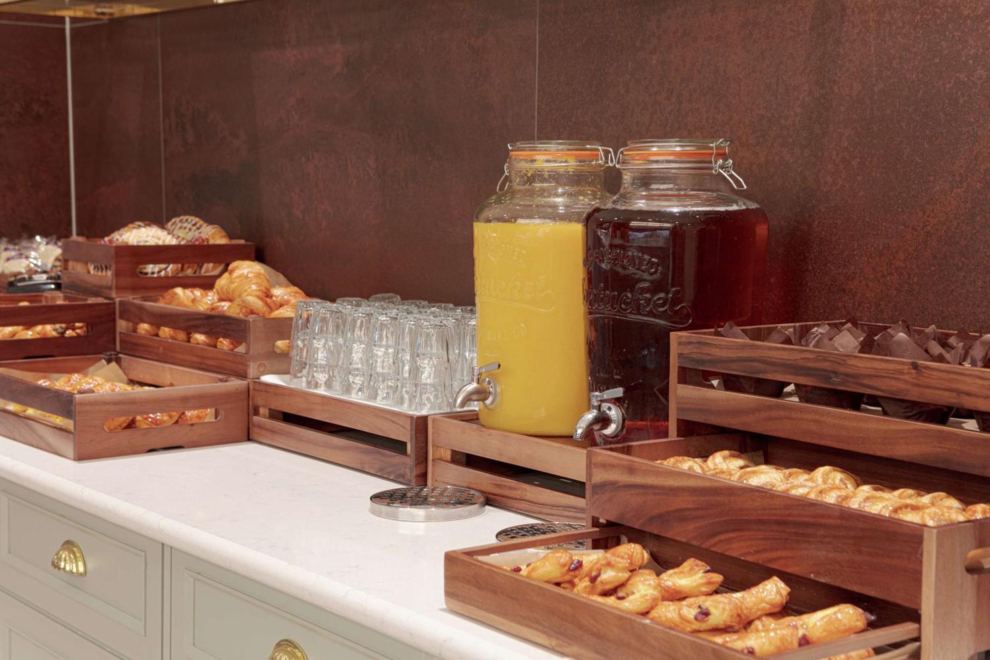 โรงแรมฮิลตัน เบลฟาสท์ เบลฟาสต์ ภายนอก รูปภาพ The photo shows a buffet-style setup featuring various food and beverage items. There are several wooden trays filled with pastries, including croissants and other baked goods. In the background, there are two large glass jars, one filled with yellow